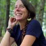 amybutlercu | Antioch University | Antioch University Smiling woman with dark hair wearing a blue shirt, outdoors among trees in a forest.