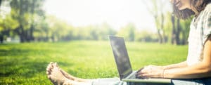 barefooted student typing on laptop outside