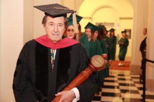 Commencement, speaker walking out to stage holding large wooden object in his arms