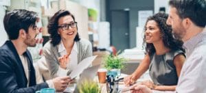 Group of four classmates or coworkers sitting at table talking