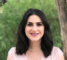 Chrystal Rahmani, Ph.D.- Woman with length dark hair and wearing a pink shirt. She is in front of trees.