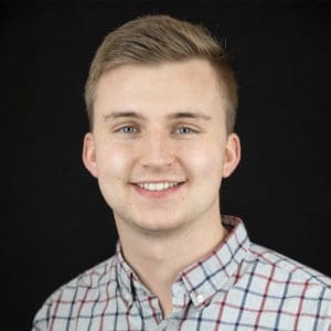 Marcus smiling in a plaid shirt against a black background