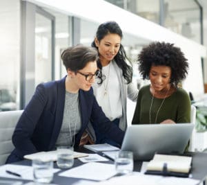 Women in leadership header image; Three individuals working together on computer