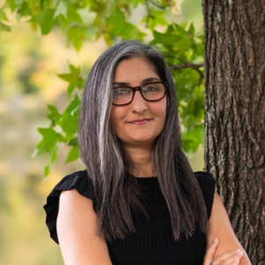 Anjali-Enjeti | Antioch University Anjali Enjeti- Woman standing in front of tree, smiling.
