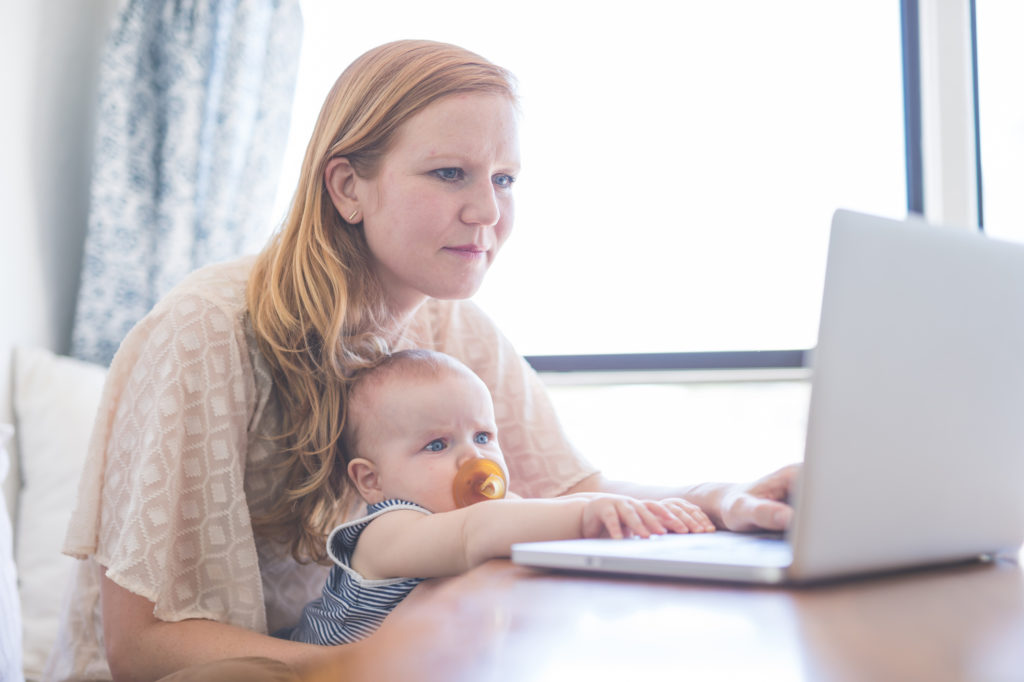 Mom works on her computer while holding her infant baby in her lap