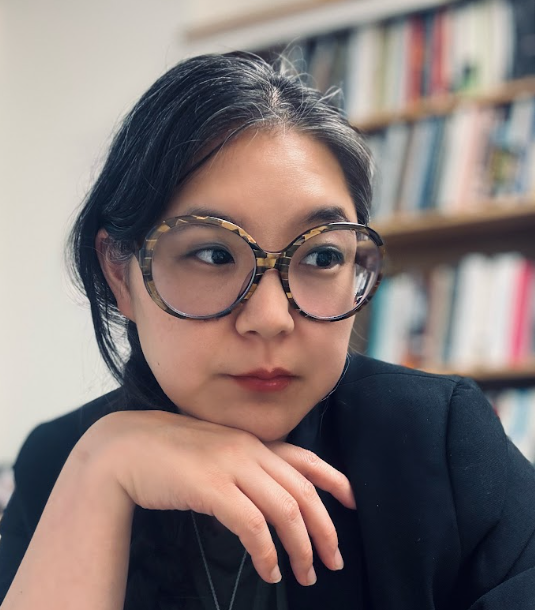 JaniceLee Antioch University Portrait of a woman with large round glasses in front of bookshelves Janice Lee