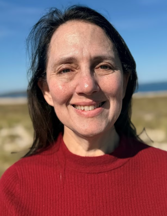 JennyFactor Antioch University Smiling woman outdoors at the beach wearing a red sweater blue sky in the background