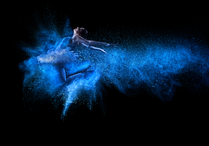 Young beautiful dancer jumping into blue powder cloud