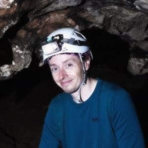 John wearing a helmet and smiling in a cave