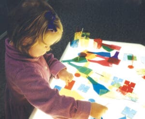 Student playing with shapes on a lightboard.