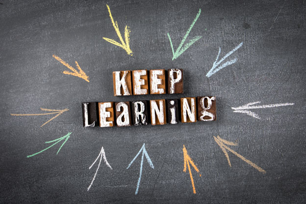 Chalkboard with multi-colored arrows pointing to letter tiles that spell out, keep learning.