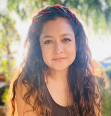 Celina Jaques- A woman with long hair and a multi-colored headband wearing a brown shirt.