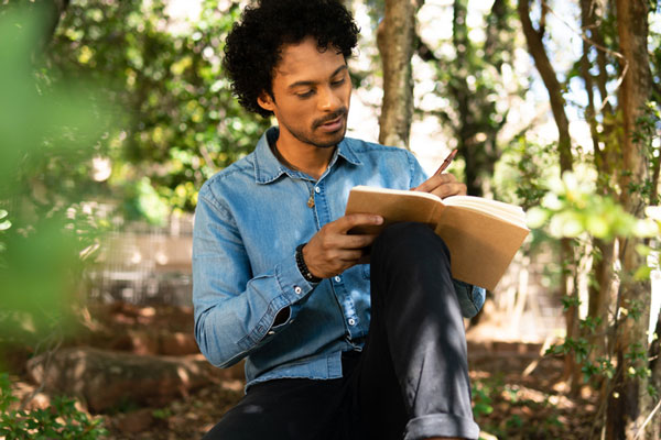 Person sitting in a forest and writing in a notebook.