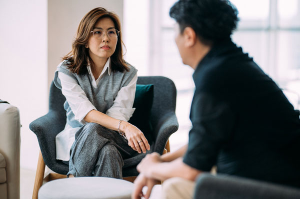 Two people talking and sitting on chairs. One with their back to the camera and the other facing the person and the camara.