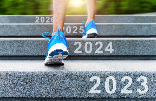 Person's feet climbing stairs. Each stair is labeled with a year, 2023, 2024, 2025...