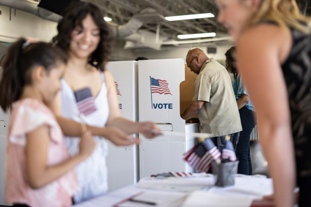 People working at a polling place talking with a woman and a child.