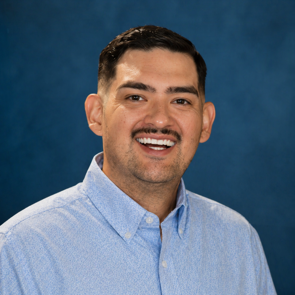 a portrait of a man smiling in a blue button up shirt and a blue background