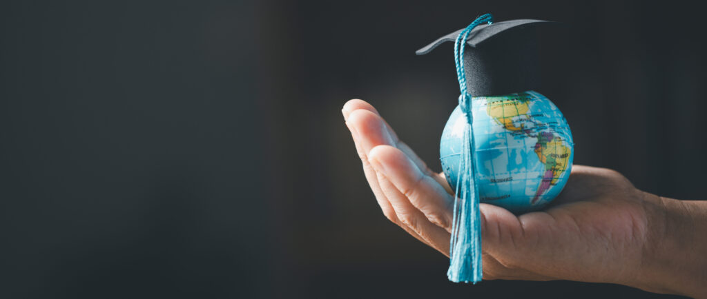Black background with a hand holding a small globe with a graduation cap on the globe.