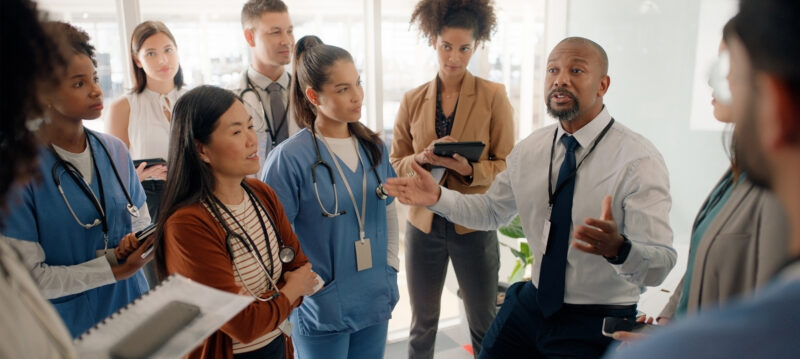 A male. hosting a meeting speaking to a myriad of nurses