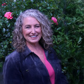 Keely-Nudo | Antioch University woman smiling in a pink shirt and jean jacket with roses behind her
