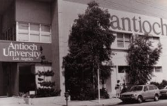 Black-and-white street view of the Antioch University Los Angeles building with trees and a parked car nearby.