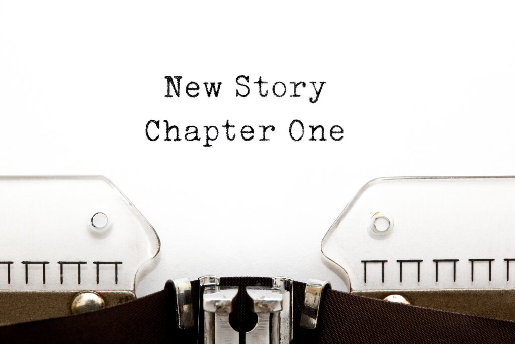 New Story Chapter One Typewriter | Antioch University Close-up of a vintage typewriter with the words 'New Story' and 'Chapter One' typed in bold, old-fashioned font on the page edge.