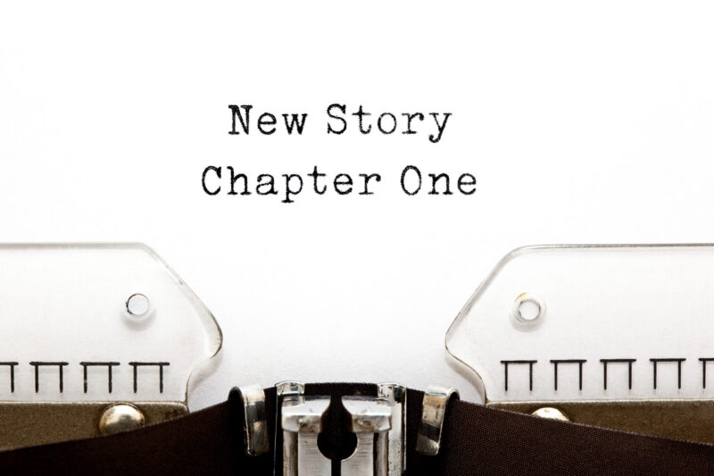 Close-up of a vintage typewriter with the words 'New Story' and 'Chapter One' typed in bold, old-fashioned font on the page edge.