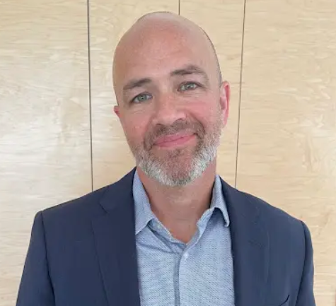 Doug Judge, person smiling at camera, wearing a blue shirt and blue jacket