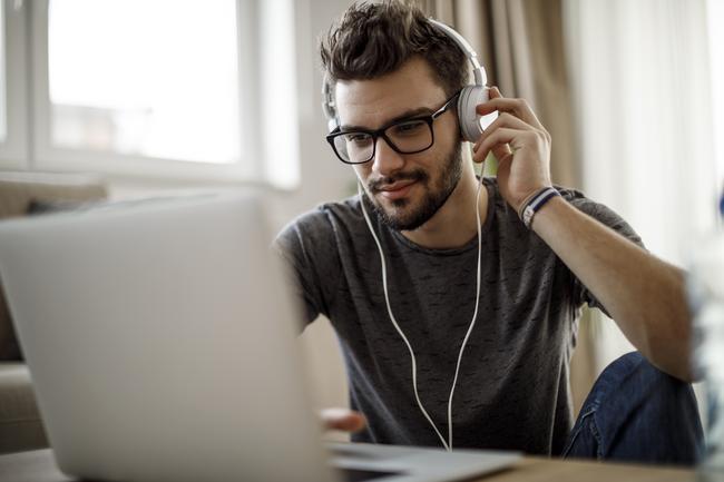Young man wearing glasses and headphones, working on a laptop at home.