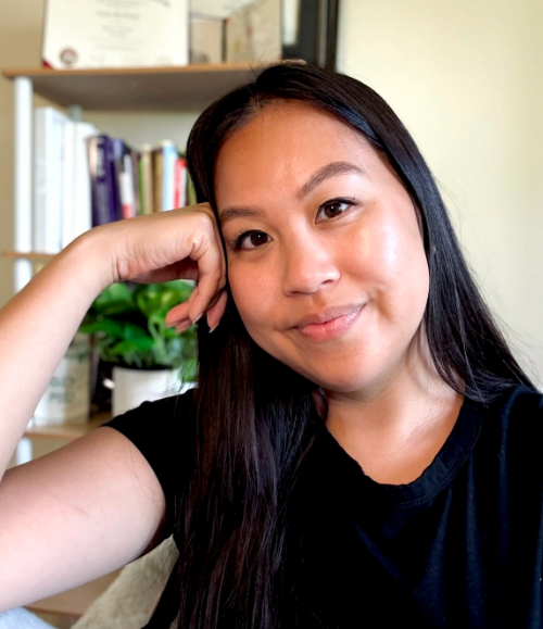 Leilani Reyes | Antioch University Leilani Reyes, smiling woman, black shirt, plant, bookshelf, books