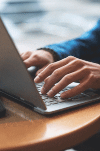 Close-up of hands typing on a laptop on a round wooden table.