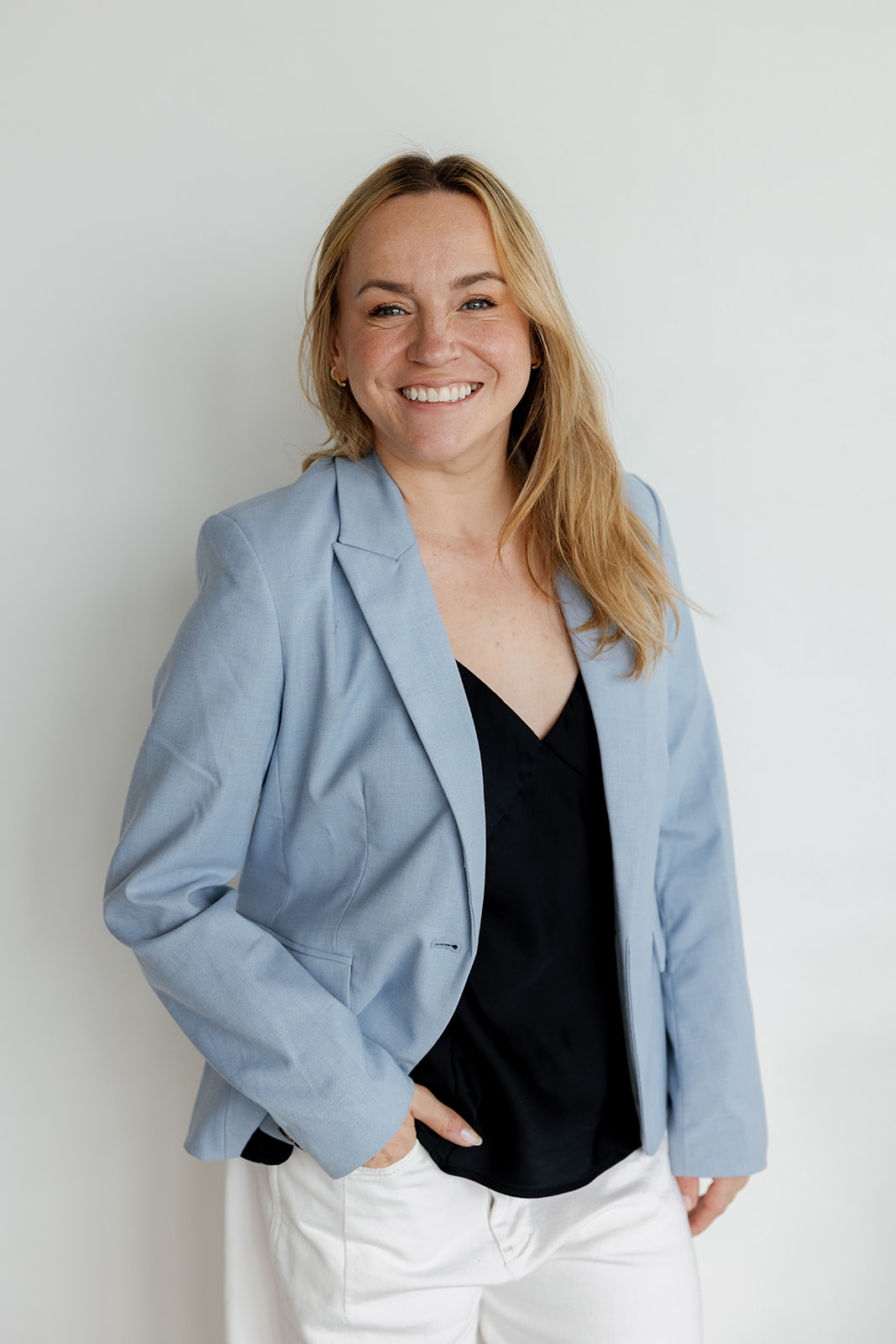 Smiling woman in a light blue blazer and black top standing against a pale wall