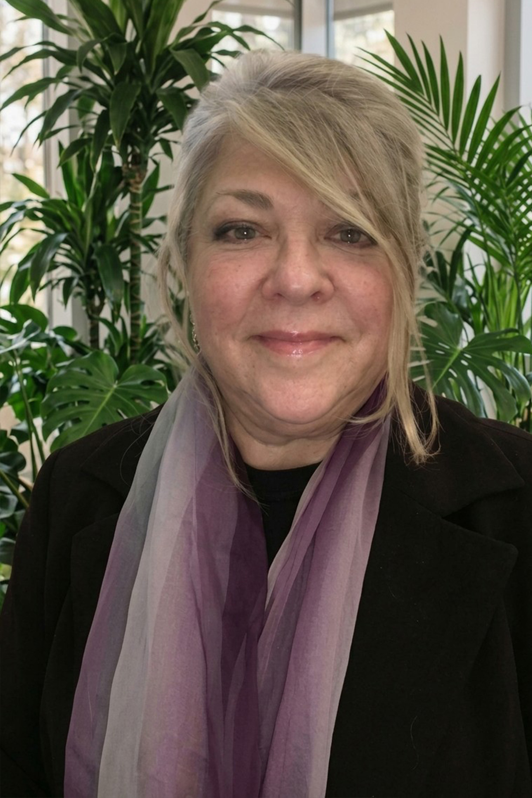 Portrait of a smiling woman wearing a purple scarf standing in front of green plants