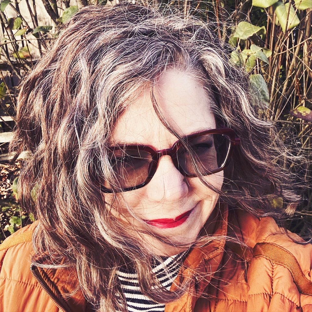 portrait of a woman smiling in a bright orange jacket and bright red lipsstick red lipstick sun glasses