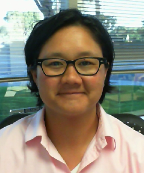 A portrait of a woman sitting in front of a window in a pink button down shirt
