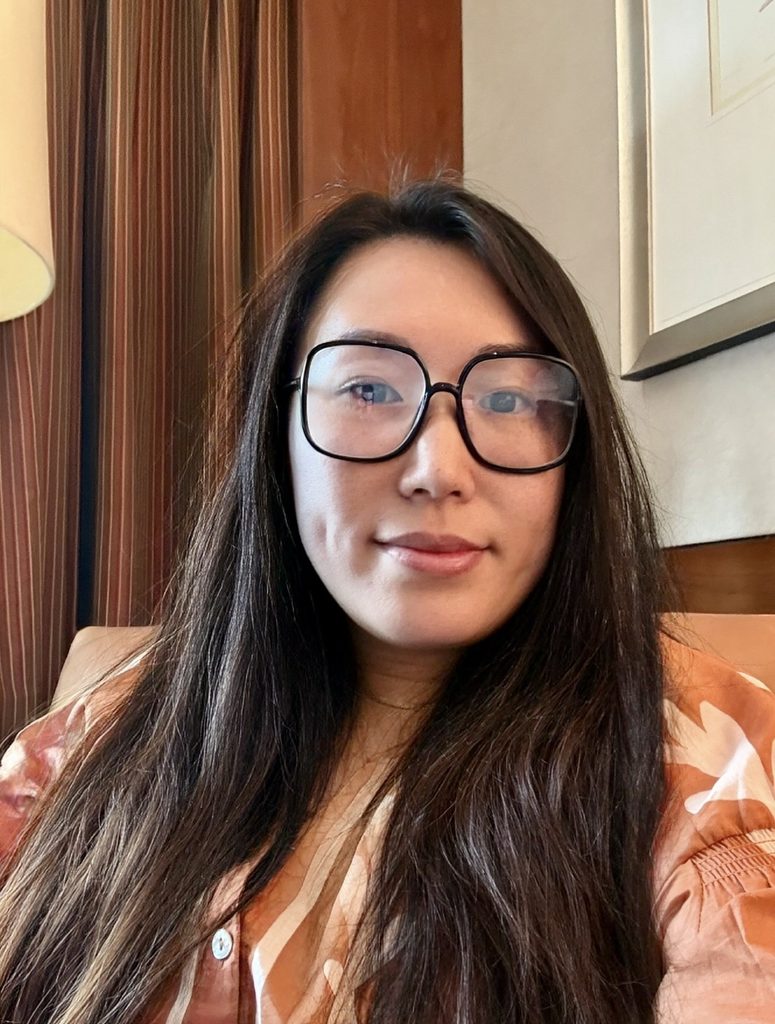 portrait of a woman with long brown hair wearing glasses in a bright orange button up shirt